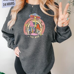 May include: A dark gray sweatshirt with a colorful mushroom graphic and the text "Stay Wild".