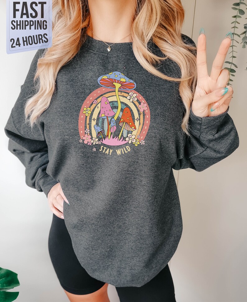May include: A dark gray sweatshirt with a colorful mushroom graphic and the text "Stay Wild".