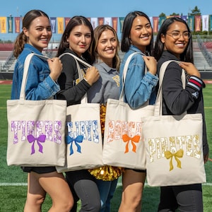 A group of five young women standing together, each holding a tote bag with a different color and text design.