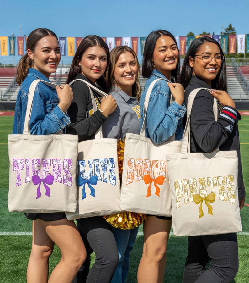 A group of five young women standing together, each holding a tote bag with a different color and text design.