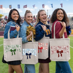 Four young women standing on a sports field, each holding a tote bag with a different word printed on it.