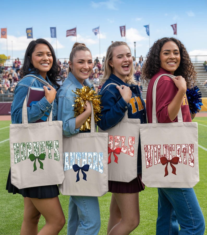 Four young women standing on a sports field, each holding a tote bag with a different word printed on it.