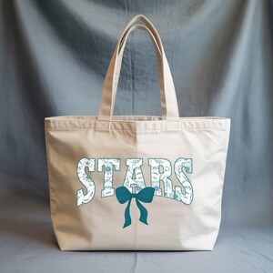 A beige tote bag with the word "STARS" printed on it, along with a blue bow.