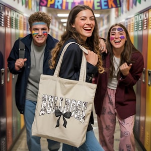 Three young people are standing in a hallway, with one of them holding a bag with the word "Bulldogs" printed on it. The other two individuals are smiling and appear to be in a cheerful mood.