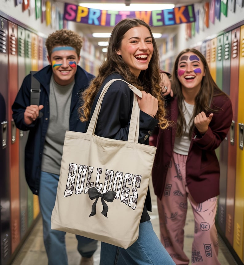 Three young people are standing in a hallway, with one of them holding a bag with the word "Bulldogs" printed on it. The other two individuals are smiling and appear to be in a cheerful mood.