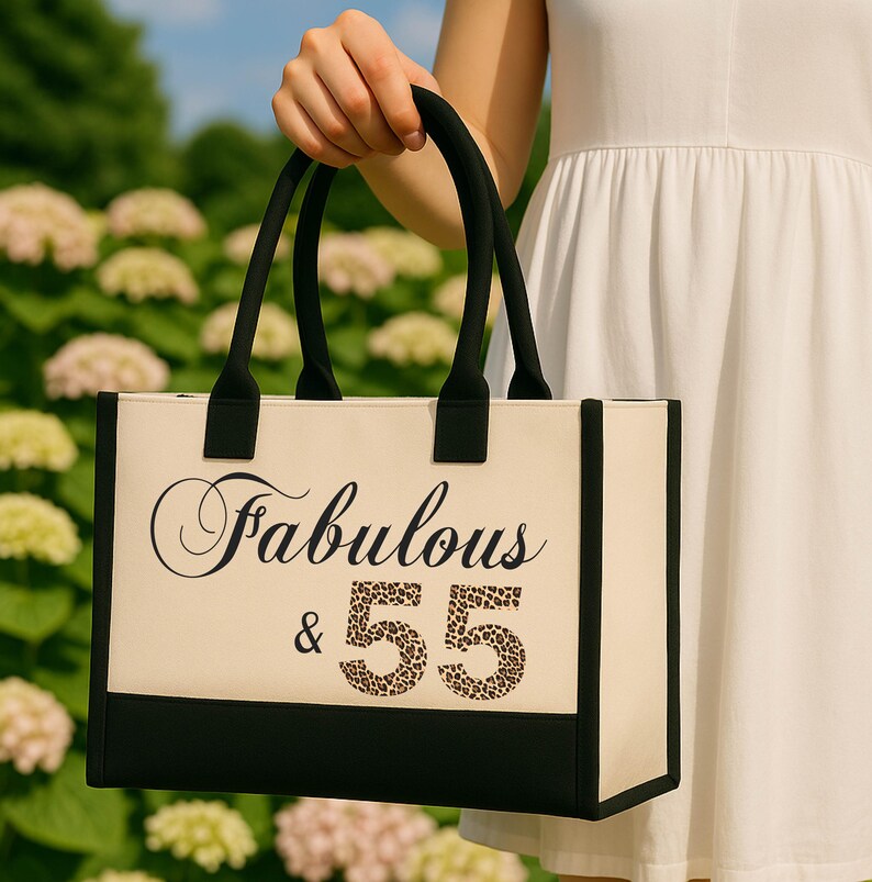 A person is holding a tote bag with the text "Fabulous & 55" printed on it.