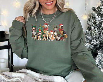 May include: An olive green crewneck sweatshirt featuring a graphic print of various dog breeds wearing Santa hats and festive accessories, including a Christmas tree and string lights, arranged in a group on the front of the garment.