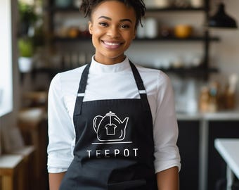 May include: A black apron featuring a white line art graphic of a teapot with a t-shirt silhouette inside the body of the pot. The word TEEPOT is printed in white capital letters directly underneath the teapot graphic on the front of the apron.
