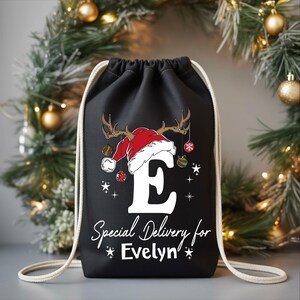 A black drawstring bag with a Christmas-themed design, featuring a Santa hat and ornaments, and the text "Special Delivery for Evelyn" printed on it.