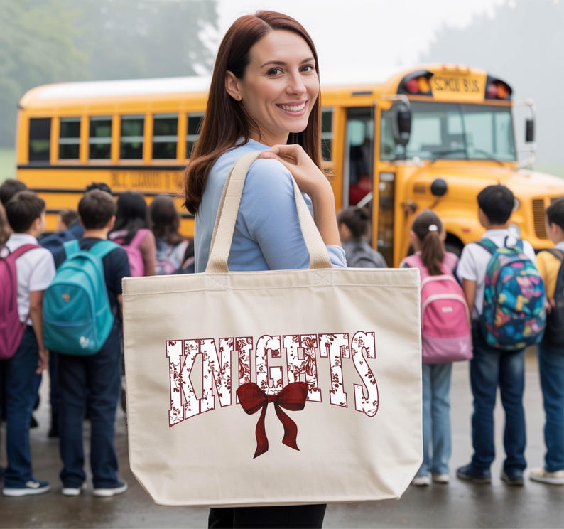 A woman holding a large tote bag with the word "KNIGHTS" printed on it, standing in front of a group of students and a yellow school bus.