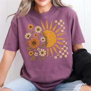 A woman wearing a purple t-shirt with a sun and flower design.