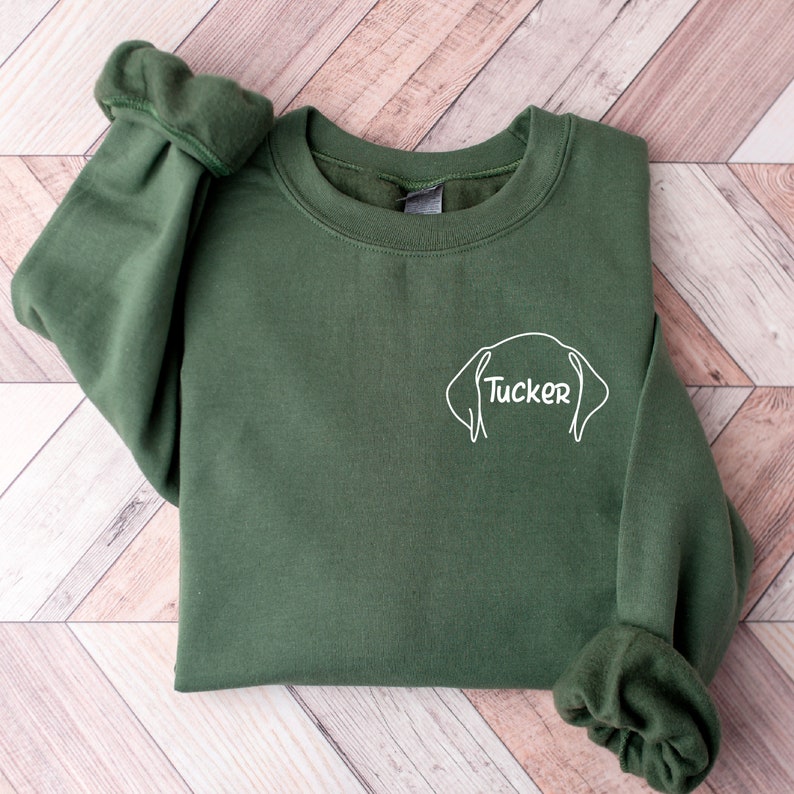 May include: A green sweatshirt with a white outline of a dog's head and the name "Tucker" written inside the outline.