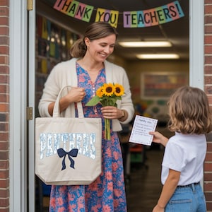 A woman in a floral dress holds a bag with the word "Panthers" and a bouquet of sunflowers, standing in front of a classroom door with a child holding a card.