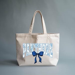 A beige tote bag with the word "PANTHERS" printed on it, along with a blue bow.