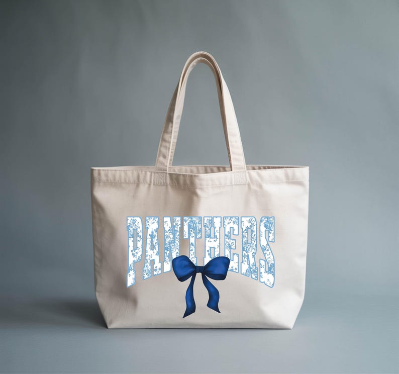A beige tote bag with the word "PANTHERS" printed on it, along with a blue bow.