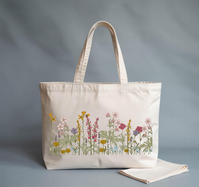 A white tote bag with a floral embroidered design on the front, featuring various colorful flowers and plants.