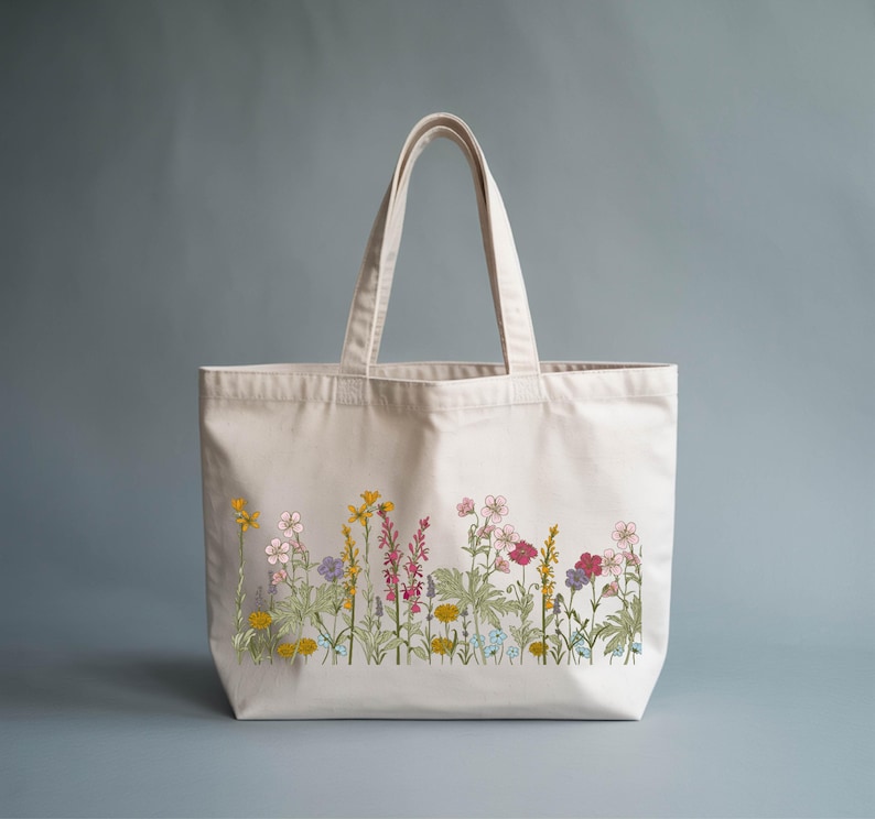 A white tote bag with a floral embroidered design on the front, featuring various colorful flowers and plants.