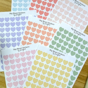 May include: A collection of sticker sheets featuring heart shapes in pastel shades like pink, yellow, green, and lilac. Each sheet is labelled with the text "Big Heart Stickers by Jubiful".