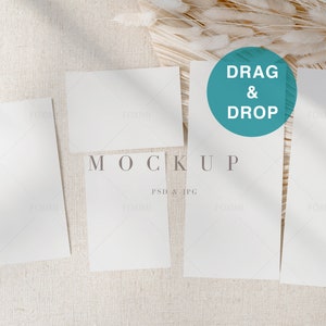 May include: Five blank white cards arranged on a beige textured surface with a dried pampas grass bundle in the background. The text "DRAG & DROP" is in a teal circle on one of the cards. The text "MOCKUP" is below the cards. The text "PSD & JPG" is below the word "MOCKUP".