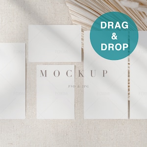 May include: Four blank white cards on a beige textured background with a dried palm leaf in the background. The cards are arranged in a rectangle shape with the text "MOCKUP PSD & JPG" in the center. The text "DRAG & DROP" is in a teal circle above the cards.