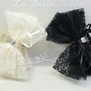 May include: Two lace hair clips, one ivory and one black, each adorned with a sparkling rhinestone and ribbon. The clips have a claw design for secure hold. The background has the text "La Belle Table".