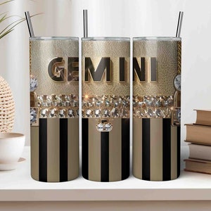 Puede incluir: Tres vasos de acero inoxidable con rayas negras y doradas. Los vasos presentan la palabra "GEMINI" en letras doradas con diamantes de imitación.