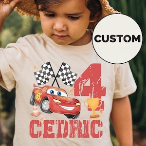 Puede incluir: Una camiseta beige con un gr&aacute;fico de coche de carreras rojo, banderas a cuadros, el n&uacute;mero 4, un trofeo dorado y el nombre "CEDRIC". La camiseta tiene un dise&ntilde;o personalizado, adecuada para un cumplea&ntilde;os infantil.