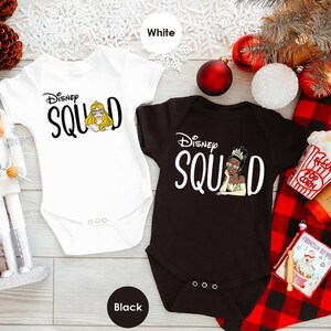 May include: Two baby onesies, one white and one black, with the text "Disney Squad". The white onesie features a graphic of Princess Aurora, and the black onesie features Princess Tiana. Both have short sleeves and three snaps at the bottom.