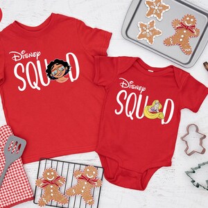 May include: Red Disney Squad t-shirts and onesie. The t-shirt features a graphic of a character with glasses, and the onesie has a princess graphic. Baking supplies and gingerbread cookies are also in the image.