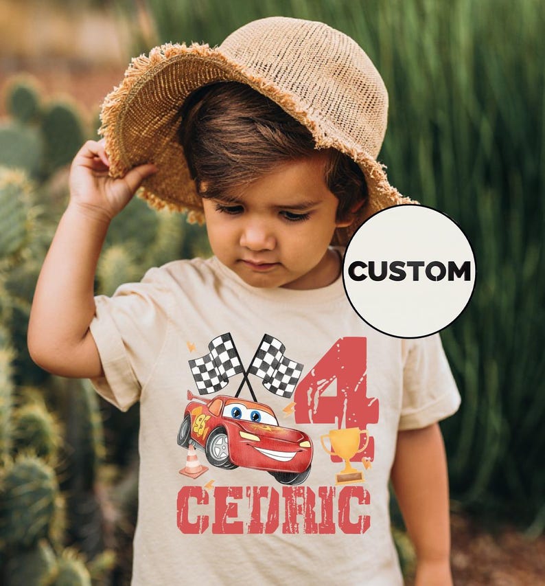 Puede incluir: Una camiseta beige con un gr&aacute;fico de coche de carreras rojo, banderas a cuadros, el n&uacute;mero 4, un trofeo dorado y el nombre "CEDRIC". La camiseta tiene un dise&ntilde;o personalizado, adecuada para un cumplea&ntilde;os infantil.