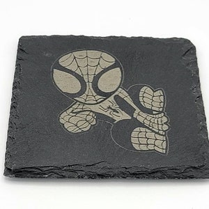 May include: A black slate coaster with a white design of a cartoon Spider-Man character.