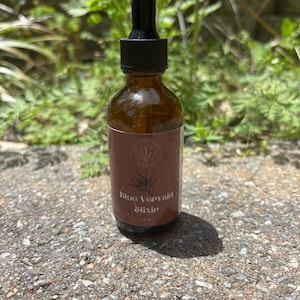 以下が含まれることがあります： 黒いドロッパー付きの茶色のガラス瓶。瓶には「Blue Vervain Elixir」とラベルが貼られています。