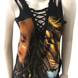 May include: Black tank top with a distressed neckline and lace-up detail. The front features a graphic of a man's face and a lion's face, with dreadlocks and a colorful bead.