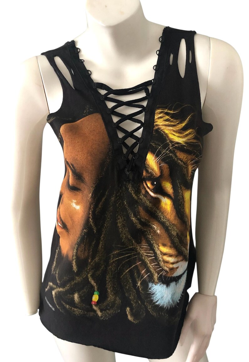May include: Black tank top with a distressed neckline and lace-up detail. The front features a graphic of a man's face and a lion's face, with dreadlocks and a colorful bead.