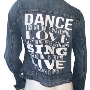 May include: A blue denim jacket with white text on the back that reads "Dance like no one is watching, Love like you've never been hurt, Sing like no one is listening, Live like heaven is on earth."