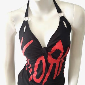 May include: Black halter top with red text. The top has a knotted front and metal ring details at the halter straps. The word "YORK" is printed in a bold, stylized font across the front.