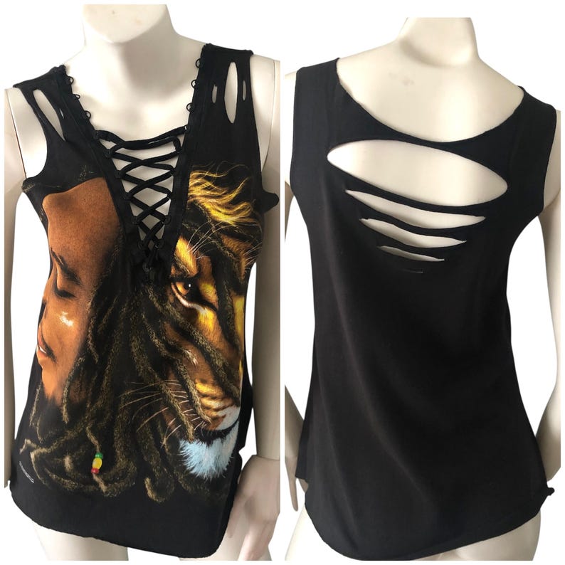 May include: Black tank top with a graphic print of a lion and a person with dreadlocks. The front features a lace-up neckline and cut-out details. The back has three horizontal cut-out slits.