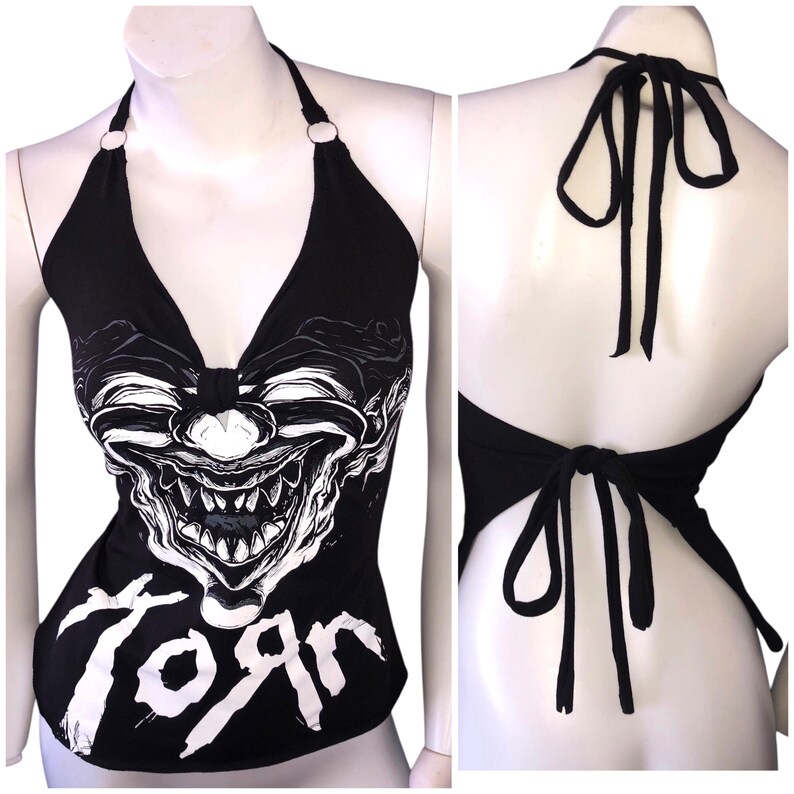 K&ouml;nnte beinhalten: Schwarzes Halstuch-Top mit einem wei&szlig;en Motiv eines gruseligen Clownsgesichts und dem Wort "Torn" auf der Vorderseite. Das Oberteil hat einen R&uuml;ckenausschnitt.