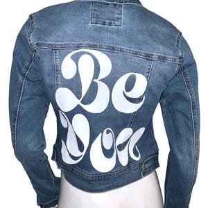 May include: A blue denim jacket with a white graphic on the back that says "Be You".