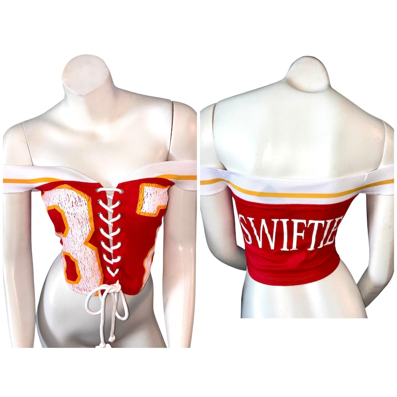 May include: Red off-the-shoulder corset top with white and yellow trim. The front features the number 87 in white with yellow outline, and a white lace-up closure. The back of the top has the word "SWIFTIE" in white.
