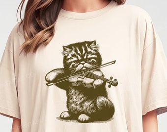 May include: A beige t-shirt with a graphic print of a cat playing the violin. The cat is brown and black and has a serious expression. The violin is brown and has a bow. The text "NATURAL" is printed in the lower right corner of the image.
