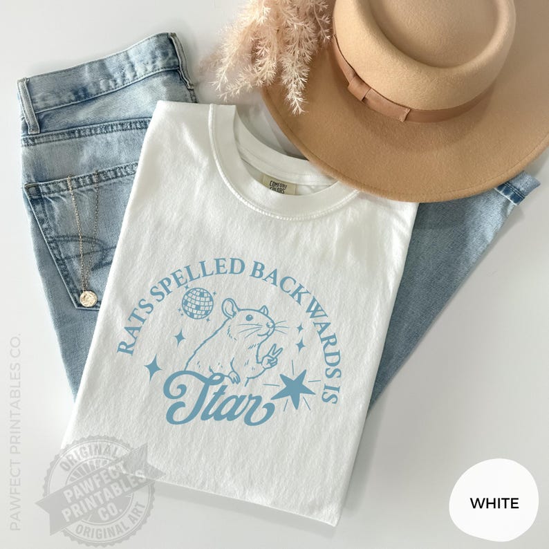 May include: White t-shirt with a light blue graphic that reads "RATS SPELLED BACKWARDS IS Star" with a rat illustration. The shirt is paired with light blue jeans and a tan hat. A gold necklace is visible.