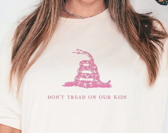 May include: A white t-shirt with a pink graphic of a coiled snake with the text "Don't Tread on Our Kids".