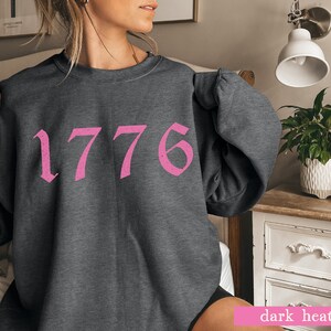 May include: A dark heather grey sweatshirt with a pink 1776 graphic printed on the front.