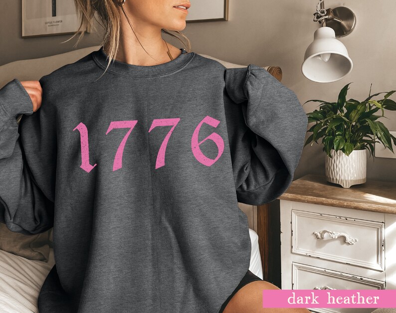 May include: A dark heather grey sweatshirt with a pink 1776 graphic printed on the front.