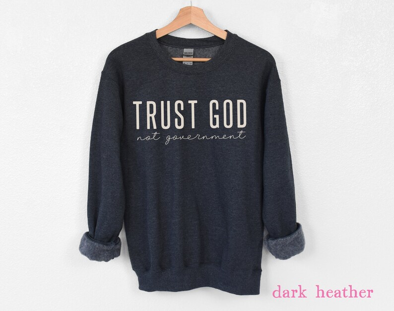 以下が含まれることがあります： 濃いグレーのヘザーのトレーナーに、白い文字で「TRUST GOD not government」と書いてあります。