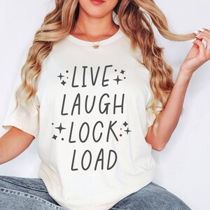 May include: A white t-shirt with the text "LIVE LAUGH LOCK LOAD" printed in black. The text is surrounded by small stars.