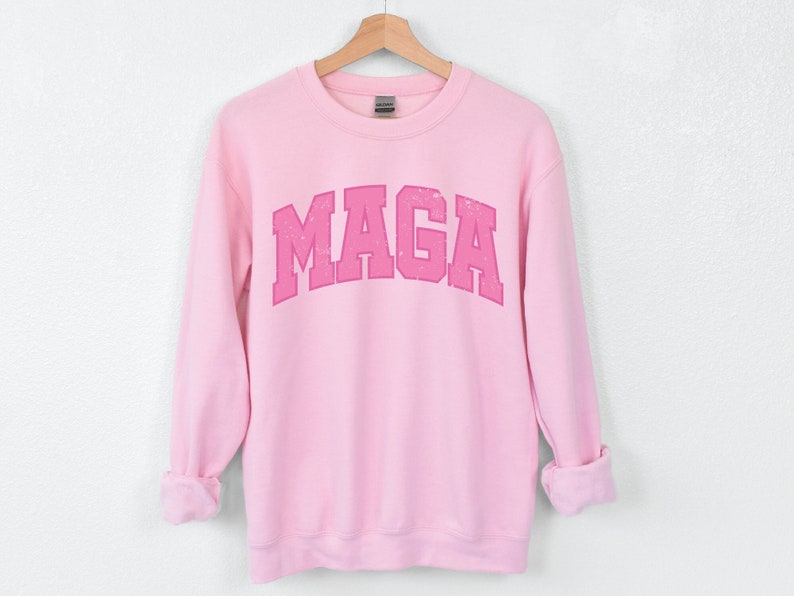 May include: Pink sweatshirt with a pink "MAGA" graphic printed on the front.