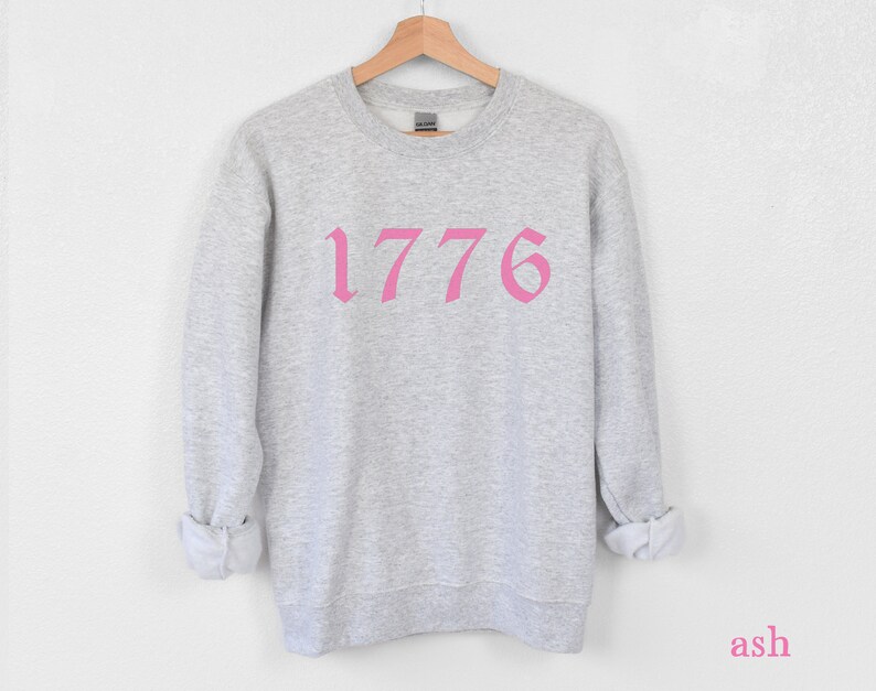 May include: A gray sweatshirt with a pink 1776 printed on the front.