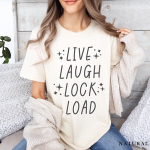 May include: A cream colored t-shirt with the text "LIVE LAUGH LOCK LOAD" in black lettering with small stars around the words.